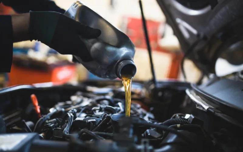 Mechanic pouring oil into car engine reservoir.