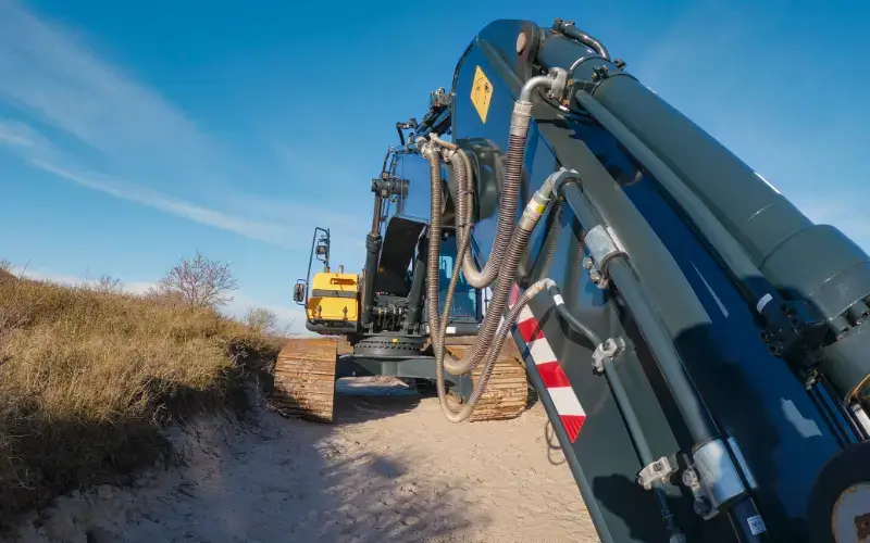 Excavator boom with hydraulic cylinders and pressure hoses.