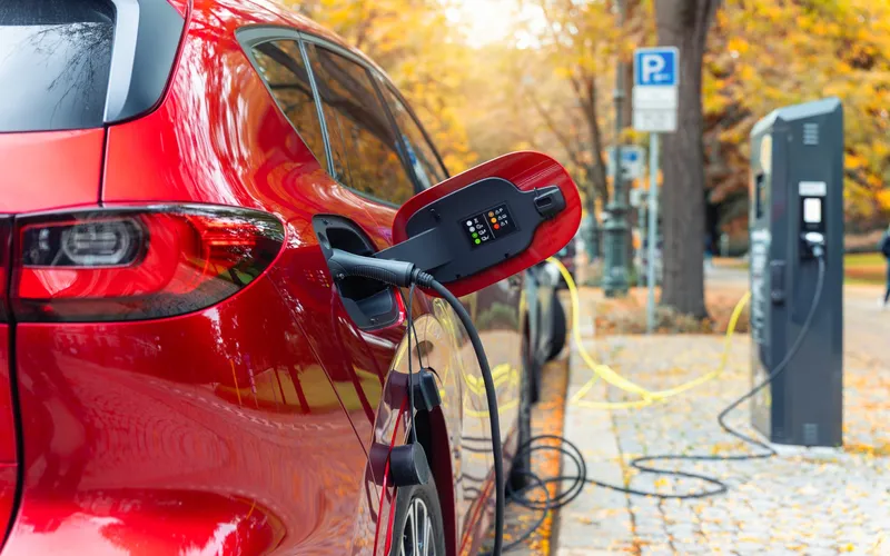 Red electric car charging on the side of the road.