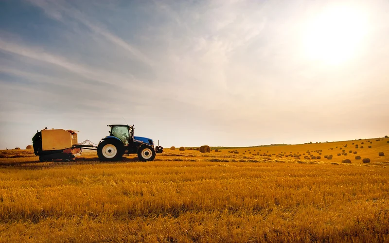 Tractor pulling baler across fields of hay.