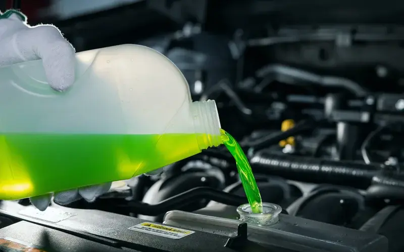 Person topping up coolant level with green fluid.