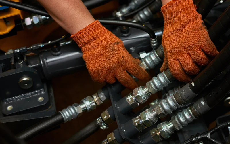 Person wearing gloves, inspecting the hydraulic system.