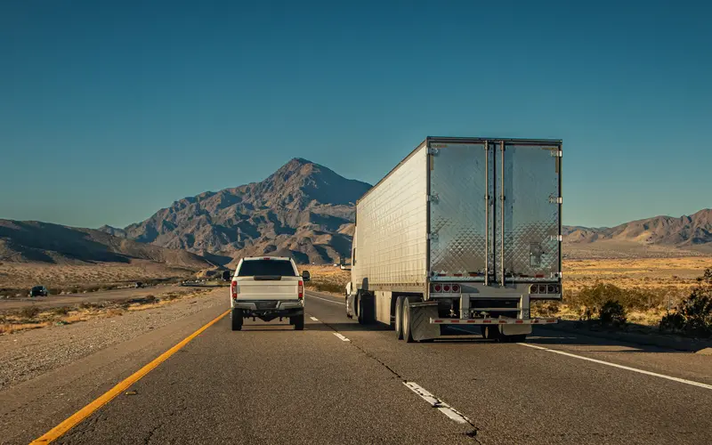 Image of truck driving next to a pickup truck on a road in the desert.