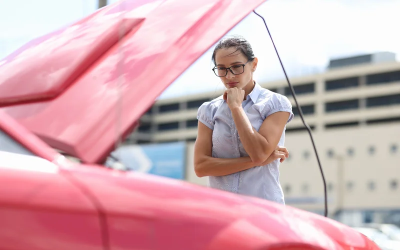 Woman looking under car bonnet at engine.