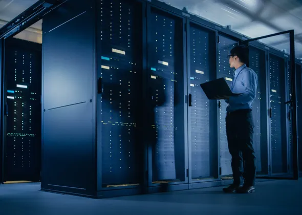 Technician holding a laptop while inspecting server racks inside a modern data center. 