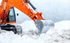 Orange excavator digging through heavy snow.