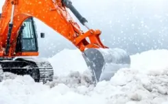 Orange excavator digging through heavy snow.