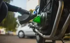 Gloved hand pouring engine oil into motorcycle engine oil reservoir.