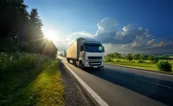 Commercial truck driving along the road between fields and trees.
