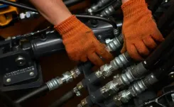 Person wearing orange gloves, inspecting the hydraulic system.